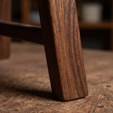 Macro shot of a hand-carved wooden chair leg, showing deep chisel marks in rich espresso walnut wood, warm workshop light