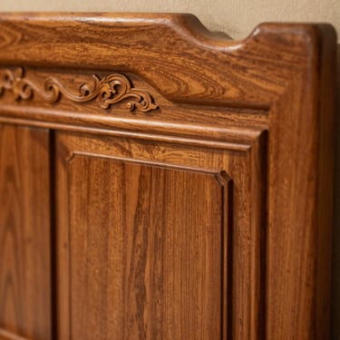 Close-up of a solid wood headboard with intricate traditional carving details, warm teak wood grain, sharp focus