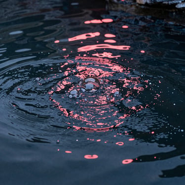 Gros plan artistique sur l'eau thermale en mouvement, capturant les bulles et les reflets de lumière rose or sur une surface sombre.