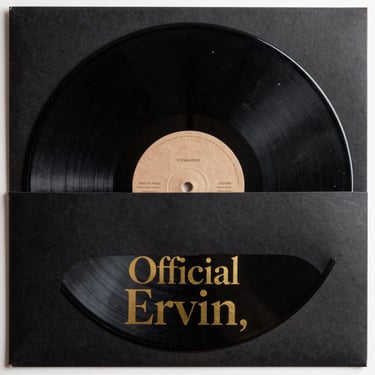 A heavy 180g black vinyl record resting half-way inside a matte black sleeve with gold leaf typography reading Official Ervin.