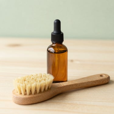 Bright editorial photography of an amber glass bottle with a wooden scrub brush on a clean wooden surface, soft diffused daylight, warm tones, shallow depth of field, 35mm