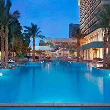 Luxury outdoor hotel swimming pool with palm trees and lounge chairs at dusk.