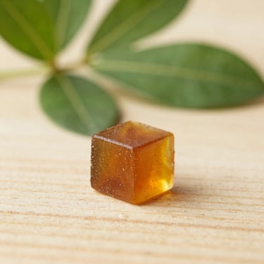 Macro close-up of amber-colored live resin concentrate on a wooden surface, soft natural daylight, shallow depth of field