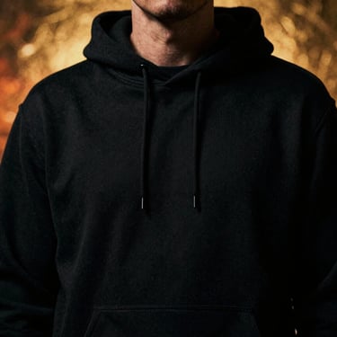 Close-up cinematic shot of a heavy black cotton hoodie, showing detailed screenprinted texture, moody low-key lighting with gold backlight.