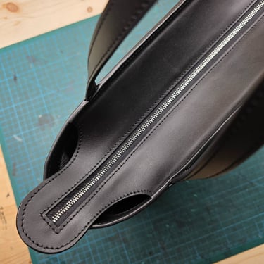 Black smooth leather tote bag with zipper closure on a cutting mat