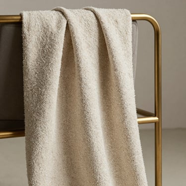 Detail of textured bouclé fabric draped over a minimalist bronze chair frame, natural side lighting