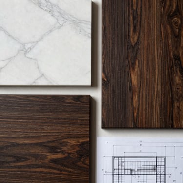 Flat lay of material palette: a block of white Calacatta marble next to a sample of dark brushed oak, architectural drafting paper