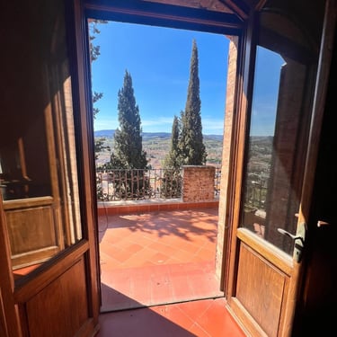 View from inside a historic property in Certaldo Alto, Tuscany, out to a private terrace with cypress trees and views