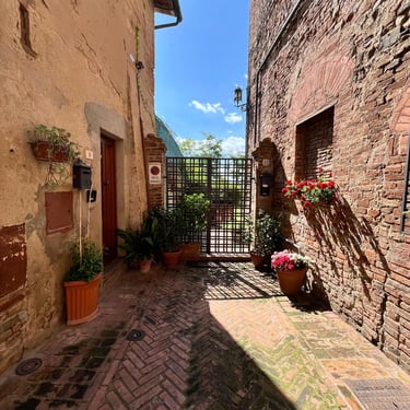 Charming historic alleyway with herringbone brick paving and potted flowers in medieval Certaldo Alto, Tuscany