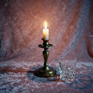 An antique bronze candle holder and a heavy crystal glass sitting on a velvet surface, soft warm lighting, cinematic shadows