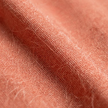 Extreme macro shot of coral-toned linen fibers under bright diffused studio light, showing the intricate warp and weft of the textile.