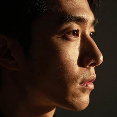 Atmospheric close-up portrait in deep shadow, soft gold light catching the profile of a face, silent and intimate