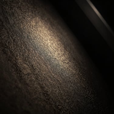Abstract extreme close-up of textured fabric in absolute darkness, illuminated by a single thin beam of light, mystical and silent.