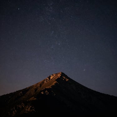 Nocturnal landscape of a lonely mountain peak under a starry dark sky, quiet crepuscular light, mystical atmosphere