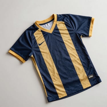 Overhead flat-lay of a youth game jersey in navy and gold on a clean light surface, natural daylight, number and side stripe visible, no props