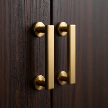 Macro close-up of a brushed gold cabinet handle mounted on dark oak wood veneer, moody studio lighting with sharp metallic highlights, shallow depth of field