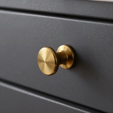 Solid brass knurled designer knob on a dark grey kitchen drawer cabinet, extreme close-up showing knurling texture and grain