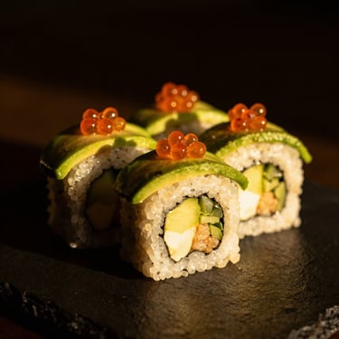 Macro shot of creative sushi rolls topped with avocado and glistening roe, warm golden-hour lighting, dark background, 50mm