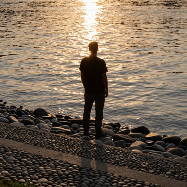 A calm, flowing river reflecting golden hour sunlight, smooth stones in the foreground.
