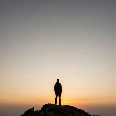 A single figure standing on a mountain peak looking at a vast, warm sunrise, expansive sky.