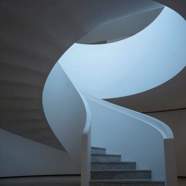 An elegant modern staircase winding upwards, clean geometric lines, soft blue light.