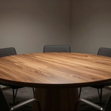 A circular wooden meeting table under soft directional light, minimalist corporate interior.