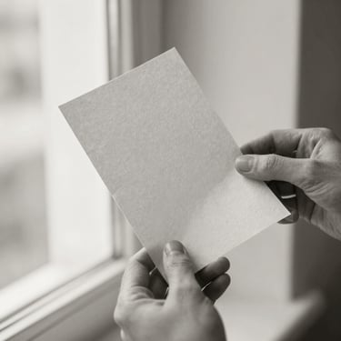 Close-up of hands holding a piece of raw, textured handmade paper, soft natural light, black and white photography, sepia undertone