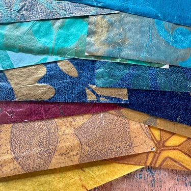 Stacked hand-painted collage papers in teal, gold, and blue tones