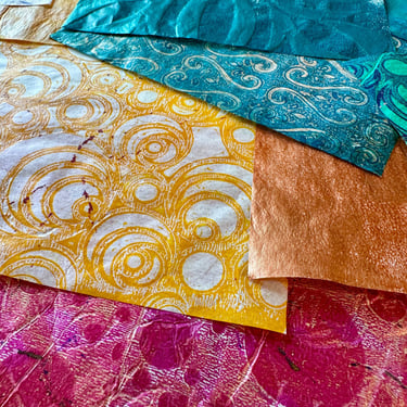 Stack of hand-painted collage papers with gold pattern and vibrant colors