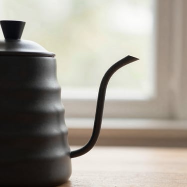 Close-up detail of a matte black precision pour-over kettle, textured steel finish, soft diffused natural daylight, minimalist composition.