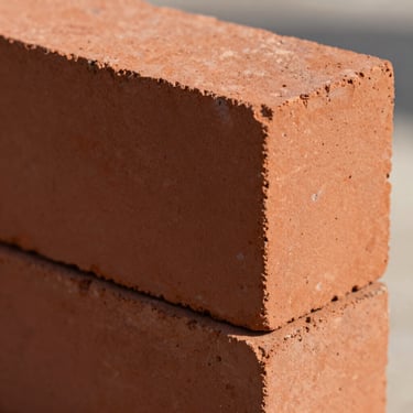 Close-up of Class II red clay brick with slightly rustic texture and rich terracotta tones under direct light.