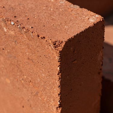 Macro close-up of Class I red clay brick showing sharp, clean edges and dense, gritty mineral texture under harsh sunlight.