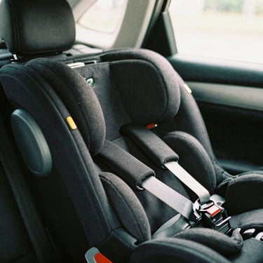 Close-up of a sturdy black rear-facing baby car seat installed securely in a car, soft window light, 35mm film look