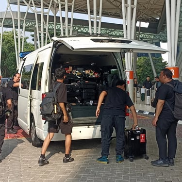 Lima orang laki-laki dewasa sedang menaikkan bagasi ke mobil Hiace warna putih.