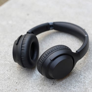 Close-up of matte black wireless over-ear headphones resting on a concrete surface, soft natural side light, sharp focus, 35mm