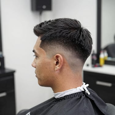 A sharp, modern fade haircut shown from the side in a bright, clean South American barber studio.