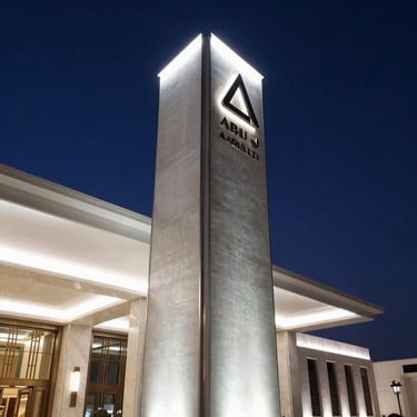 Crisp night architectural photograph of a luxury hotel entrance in Abu Dhabi, showcasing an illuminated architectural pylon sign with brushed steel finish and soft white halo lighting.