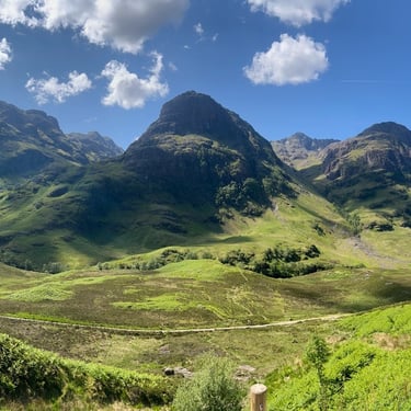 Three hills under a blue sky with green grass in the foreground