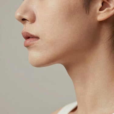 A close-up shot focusing on the elegant profile of a person's jawline and neck under soft, diffused studio lighting, emphasizing clean lines and natural skin texture.