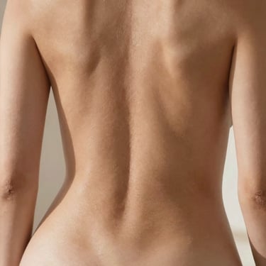A clean, artistic shot showing the elegant curvature of a person's back and waist, with soft shadows and natural daylight highlighting healthy skin tone.