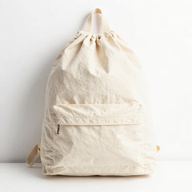 Bright high-key product photography of a cotton drawstring backpack lying flat, rich fabric textures, clean white background, 50mm