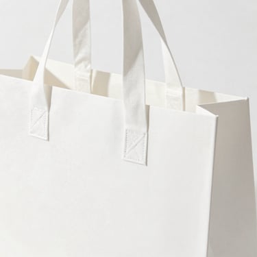 Bright high-key product photography of a premium retail shopping bag with long handles, clean white background, soft natural daylight, 50mm