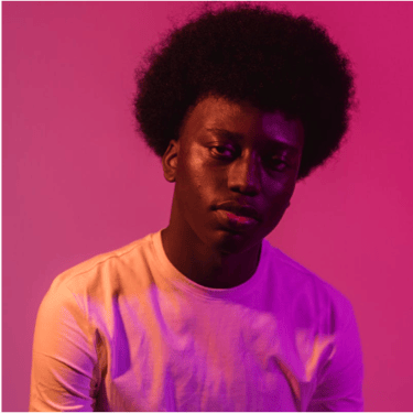 Portrait of a young Black man with an afro hairstyle under vibrant pink and purple studio lighting.
