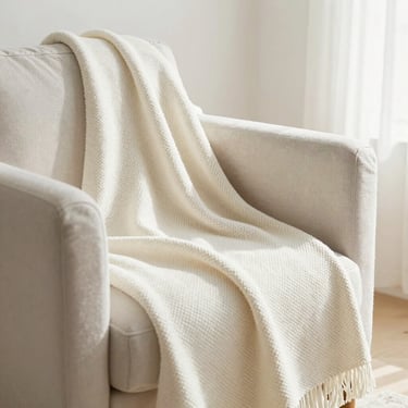 A cozy living room corner featuring a soft woven throw blanket over a modern armchair, warm daylight.