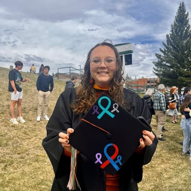 Baylie Phillips at graduation holding out her cap that is painted with 6 awareness ribbons.