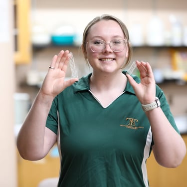 Baylie Phillips holding 3D printed polymer stents in each hand in a laboratory.