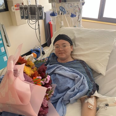 Baylie Phillips in hospital bed with flowers on her lap and ICU machines in the background.