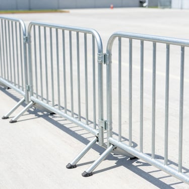 Bright outdoor commercial shot of interlocking boundary construction barriers connected in a secure line, high-key natural daylight, sharp focus on the steel frame, 35mm lens