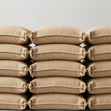 Close-up of neatly stacked premium jute bags showing organic fiber texture, bright high-key studio lighting, neutral light gray background.