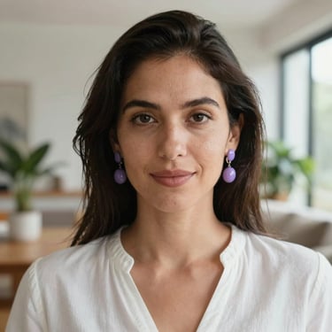 A close-up portrait of a woman with a gentle expression, wearing a simple white blouse and delicate purple earrings. She is in a bright, modern South American apartment with soft focus greenery in the background.